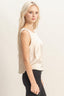 Woman wearing a beige sleeveless top and black pants against a plain background
