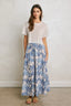 Woman wearing a white top and blue floral skirt against a plain background
