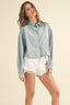 Woman wearing a light blue denim shirt and white shorts on a beige background