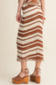 Person wearing a brown and white striped skirt with wooden clogs on a beige background