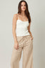 Woman wearing a white ribbed tank top and beige striped pants on a plain background