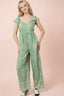 Woman wearing a green patterned jumpsuit on a pink background