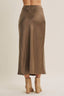 A person shown from the back wearing a flowing midi skirt in a warm taupe-brown color, paired with beige ankle boots, against a plain light beige studio background.