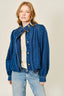 Woman wearing a blue denim jacket over a white lace top and jeans on a beige background