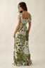 Woman wearing a floral dress with green and white pattern on a plain background