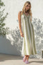 Woman wearing a green and white striped dress standing against a white wall with a plant to the left.