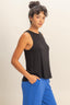 Woman wearing a black sleeveless top and blue pants against a beige background