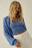 Woman wearing a blue knitted sweater and white pants against a plain background