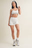Woman wearing a white sports bra and shorts set on a plain background