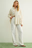 Woman wearing a light-colored shirt and white pants on a plain background