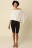 Woman wearing a white knitted poncho and black pants on a beige background