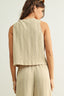Woman wearing a beige sleeveless top and pants on a light background