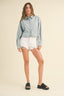 Woman wearing a light blue denim shirt and white shorts on a beige background