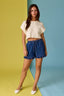 Woman wearing a white top and blue shorts on a two-tone yellow and blue background