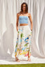 Woman wearing a blue checkered top and a colorful beach-themed skirt against a white curtain background.
