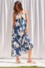 Woman wearing a blue floral dress standing against a white curtain.
