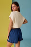Woman wearing a beige top and blue shorts against a multicolored background