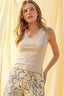 Woman wearing a beige tank top and floral skirt against a yellow curtain background