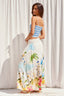 Woman wearing a colorful dress with a palm tree design against a white curtain background