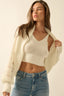 Woman wearing a cream knit cardigan over a matching top and blue jeans on a plain background