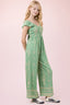 Woman wearing a green patterned jumpsuit on a pink background