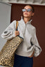 Woman wearing a gray sweater and sunglasses, holding a leopard print bag.
