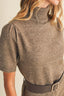 Close-up of a woman wearing a taupe brown short-sleeve knit mock neck sweater with puffed shoulders and a dark belt.