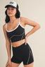 Woman wearing a black sports bra and shorts with a white cap on a beige background