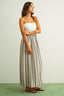 Woman wearing a white strapless top and striped maxi skirt on a plain background