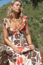 Woman wearing a floral dress sitting outdoors with greenery in the background