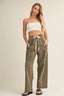 Woman wearing a white strapless top and olive green pants on a beige background
