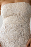 Close-up of a strapless white lace dress with floral patterns.