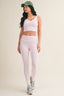 Woman wearing a pink sports bra and leggings with a green cap on a beige background