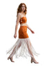 A woman walking on a city street wearing a rust-orange sleeveless crop top and matching skirt with a long cream fringe hem, paired with beige heeled sandals.