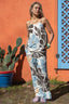 Woman wearing a floral jumpsuit standing in front of a colorful wall with a cactus plant.