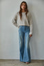 Woman wearing a light sweater and blue jeans against a plain background