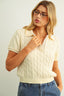 Woman wearing a cream cable knit sweater and blue jeans against a plain background