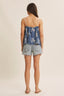 Woman wearing a blue top with white patterns and denim shorts on a beige background