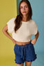 Woman wearing a beige top and blue denim shorts against a multicolored background