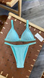 Turquoise bikini set on a woven chair with a wooden floor background