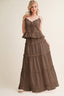 A woman modeling a brown tiered maxi dress with ruffle trim and spaghetti straps against a plain beige studio background.