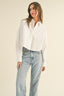 Woman wearing a white blouse and light blue jeans against a beige background