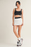Woman wearing a black sports bra and white shorts on a plain background