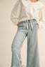 Person wearing a white blouse with a ruffled collar and light blue jeans on a beige background