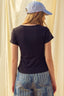 Person wearing a black t-shirt and blue cap with a beige curtain background