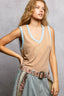 Woman wearing a beige sleeveless top with blue trim and a patterned belt against a gray background