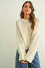 Woman wearing a cream knitted sweater and blue jeans against a plain background
