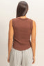Woman wearing a brown sleeveless top and gray pants on a beige background