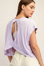 Woman wearing a light purple top with a back cutout on a plain background