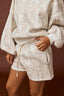 Person wearing a beige camo sweatshirt and shorts set against a brown background